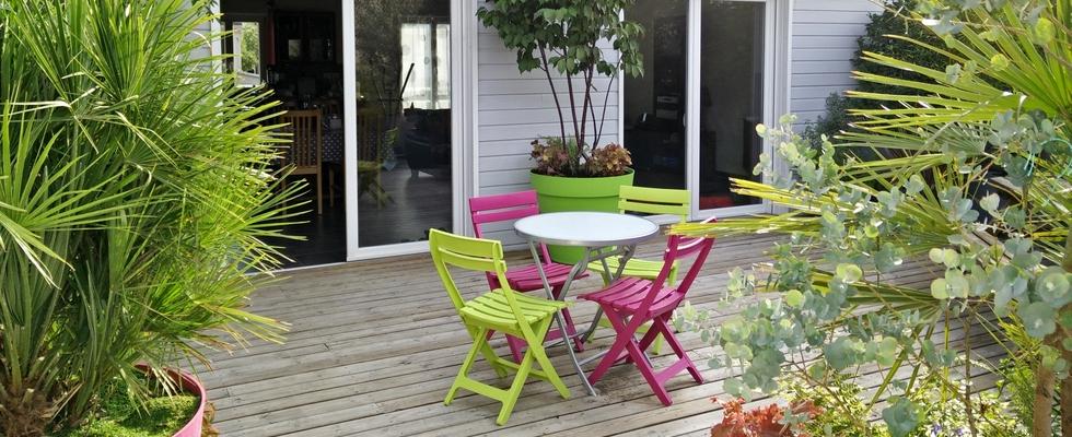 Terrasse en lames de bois, bardage peint, baies vitrées, table et chaises de jardin.